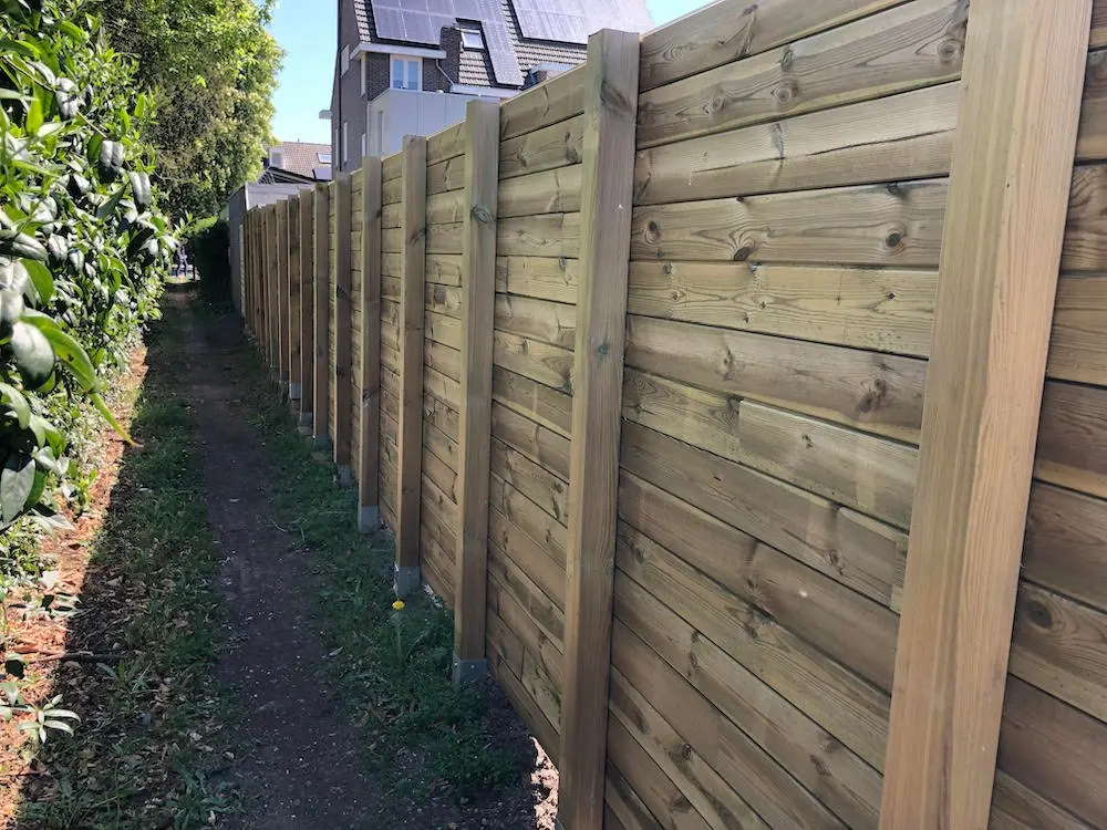 Treated MicroShades timber posts supporting a long wooden boundary fence panel system along a garden pathway.