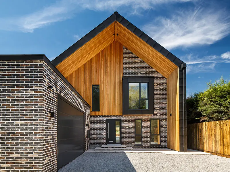 Installed vertical Siberian Larch cladding boards with a tongue and groove (T&G) profile featured under the deep gabled roof soffit and entryway section of a modern brick house.