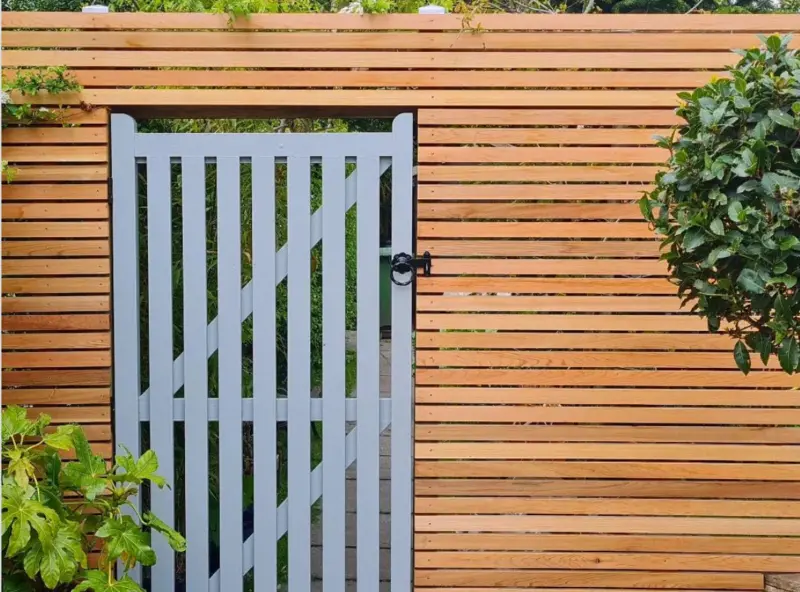 Modern horizontal slatted timber fencing panel with an integrated light grey pedestrian gate built using Ecowood Batten Screen Fencing Ease Edge 94x18mm by 3000mm length.