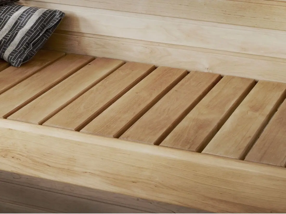 Installed Natural Alder sauna wood bench boards arranged in parallel slats alongside a matching timber paneled wall inside a sauna room.