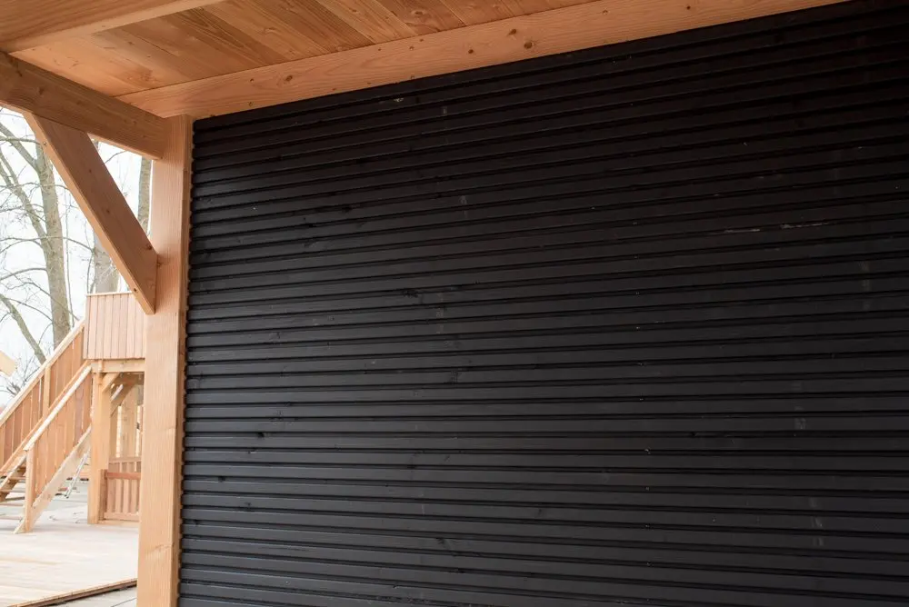 Installed black Douglas Fir cladding boards with a triple slatted profile featured as an accent wall under a natural wood sheltered structure.