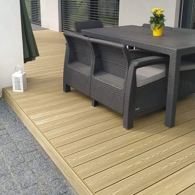 Installed PuraPrime round hollow composite decking boards in Oak featured on an outdoor patio terrace dining area with a grey rattan table and chair set.