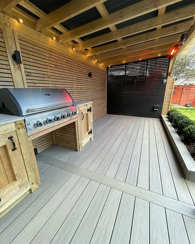 Installed PuraShield round hole co-extruded composite decking in Light Grey featured on a sheltered outdoor patio area with a built-in barbecue station and slatted timber wall panels.